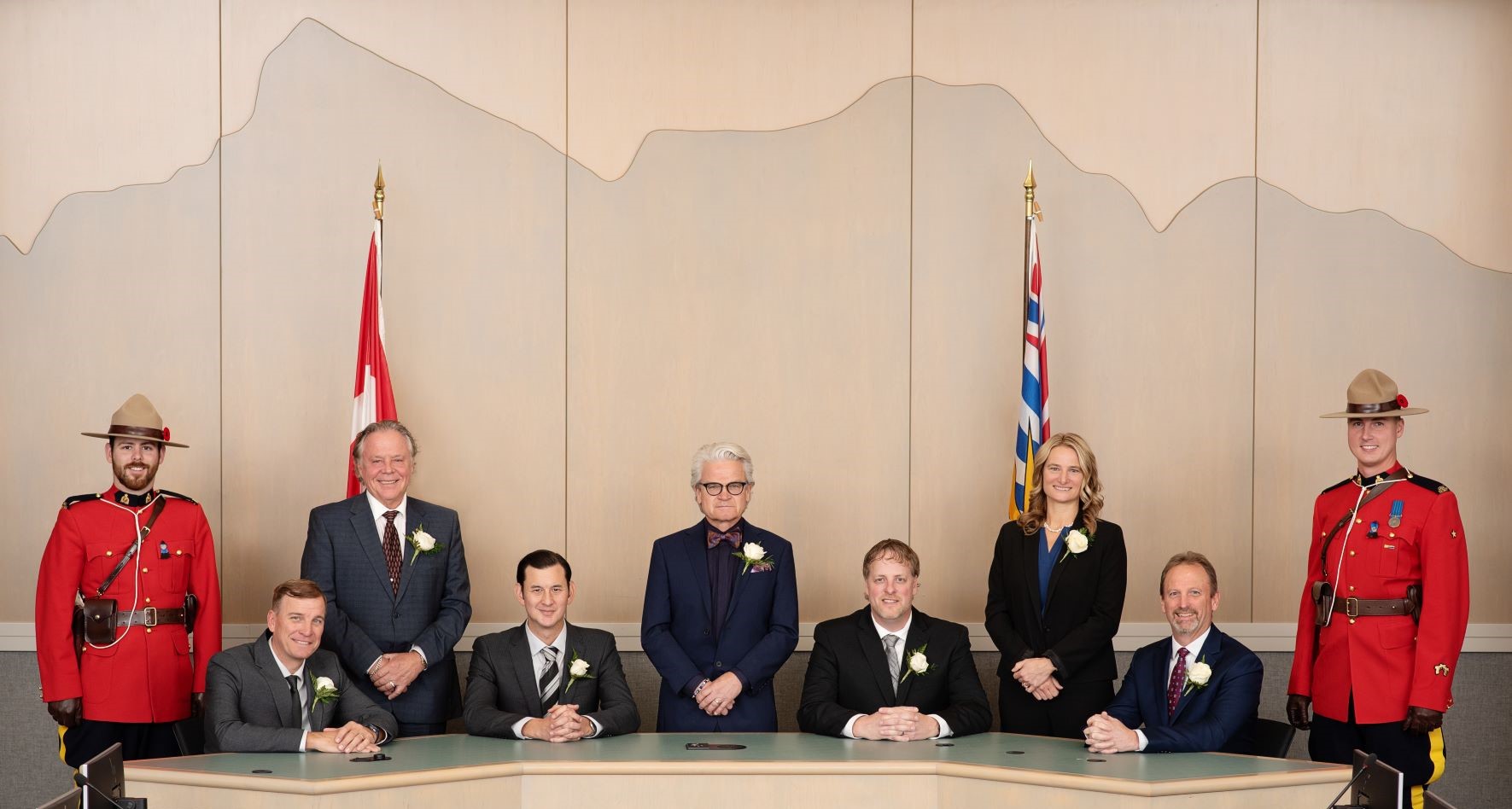 Mayor and Council in Council Chambers, with an RCMP officer in red serge on either side.
